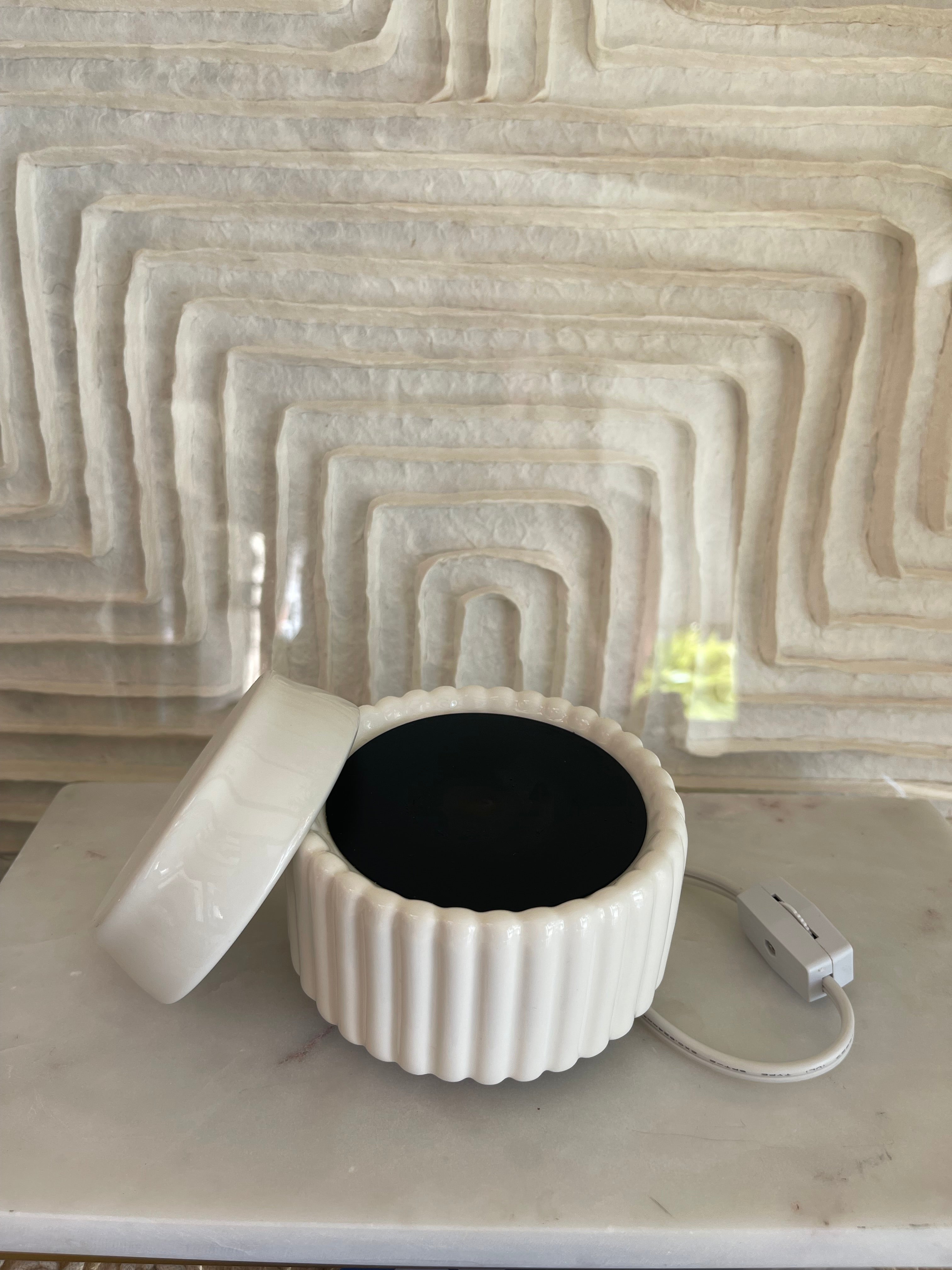 White ceramic pitcher with a black interior against a textured beige wall.